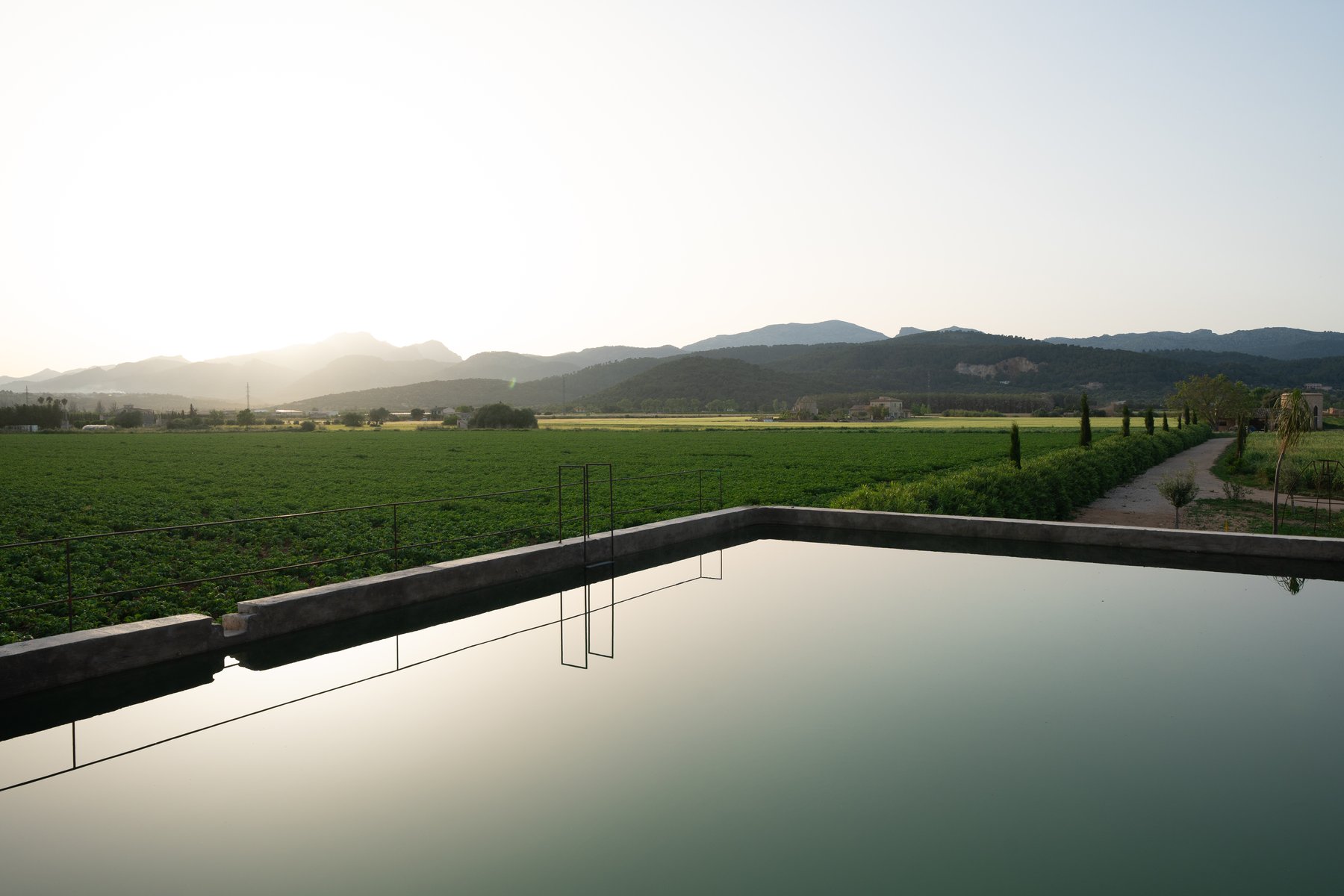 Infinity pool reflecting a green countryside landscape at dusk